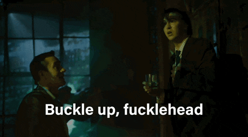 a man in a suit holds a glass and says buckle up fucklehead in white letters