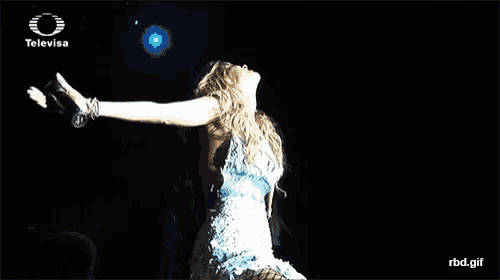 a woman in a blue dress is standing on a stage with her arms outstretched in front of a televisa logo .