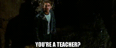 a man is standing in the dark with the words `` you 're a teacher '' written on the screen .