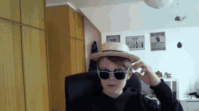 a young boy wearing a hat and sunglasses in front of a wanted poster