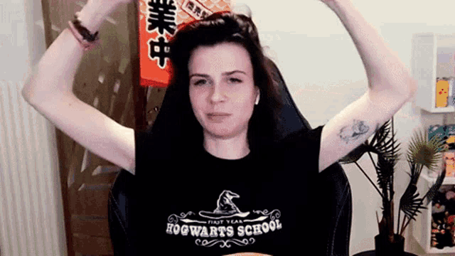 a woman is sitting in a chair wearing a hogwarts school t-shirt