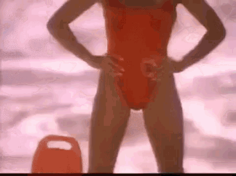 a woman in an orange swimsuit is standing on a beach next to a life preserver .