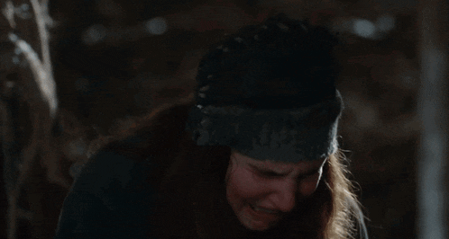 a woman wearing a beanie and gloves is kneeling down in a dark room