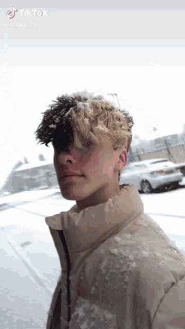 a young man is standing in the snow wearing a tan jacket .