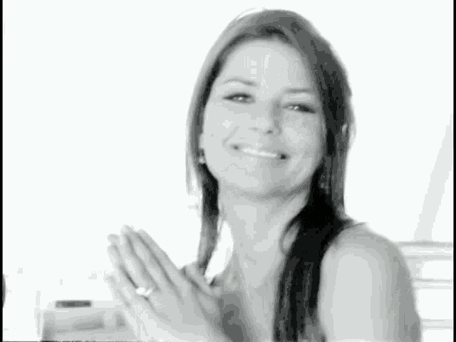 a woman is smiling in a black and white photo while holding her hands together .