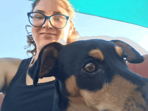 a woman wearing glasses and a black tank top holds a black and brown dog