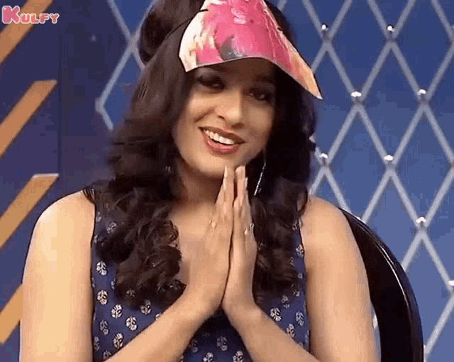 a woman wearing a pink hat and a blue dress is smiling and praying .