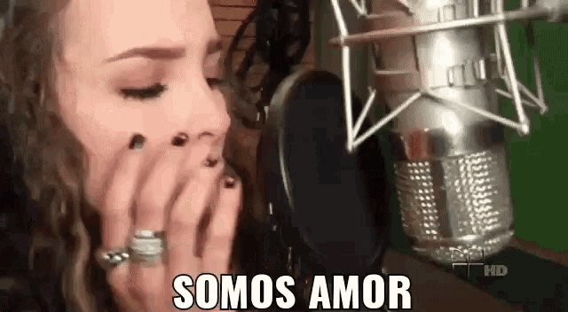 a woman is covering her mouth in front of a microphone and the words somos amor are on the screen