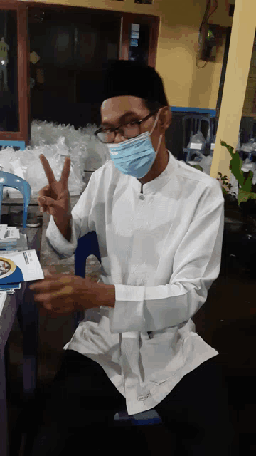 a man wearing a face mask and glasses giving a peace sign