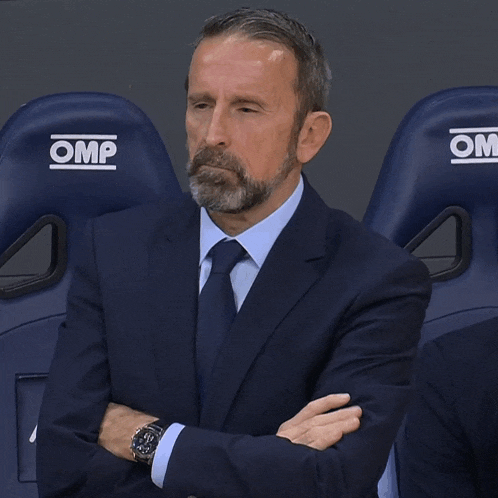 a man in a suit and tie sits in a row of omp seats