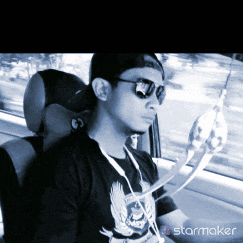 a man wearing sunglasses is sitting in a car with a starmaker logo on the bottom right