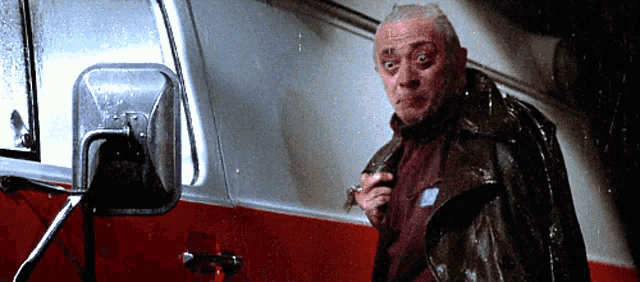 a man in a leather jacket stands in front of a red van