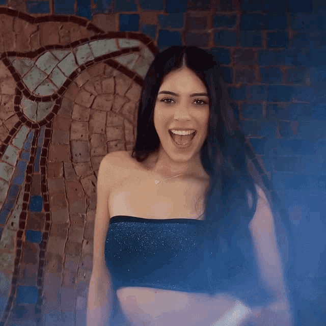 a woman in a black crop top is smiling in front of a mosaic wall