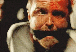 a man with blood on his face is sitting in a chair with duct tape on his mouth .