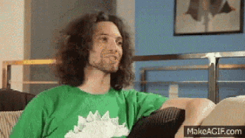 a man wearing a green shirt with a dinosaur on it is sitting on a couch
