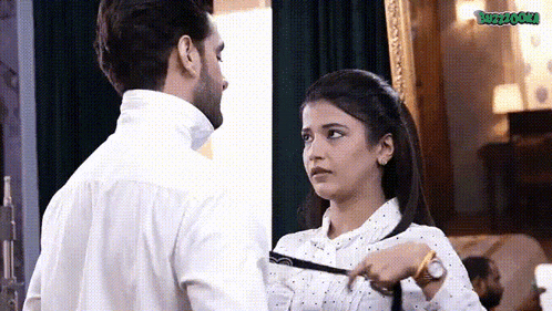 a man and a woman are standing next to each other in a room and the woman is tying the man 's tie .