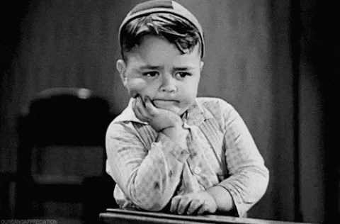 a black and white photo of a young boy leaning on a table with his hand on his chin .