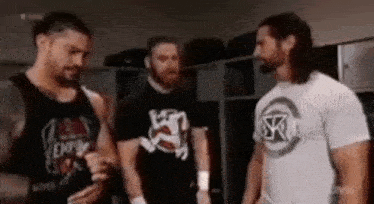 three wrestlers are standing next to each other in a locker room talking to each other .