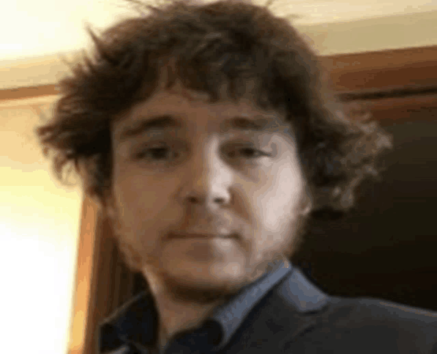 a man with curly hair and a beard is wearing a suit and blue shirt .