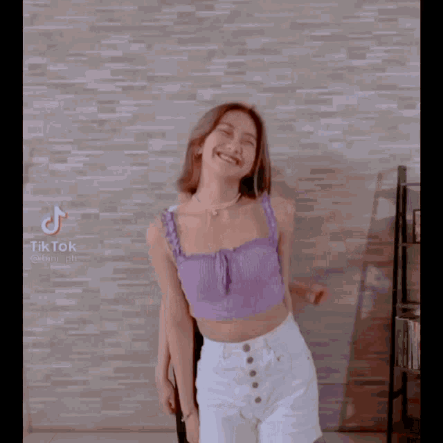 a woman in a purple top and white shorts has a tiktok icon on the bottom right