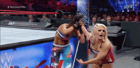two women are wrestling in a wrestling ring and one is holding the other 's head .