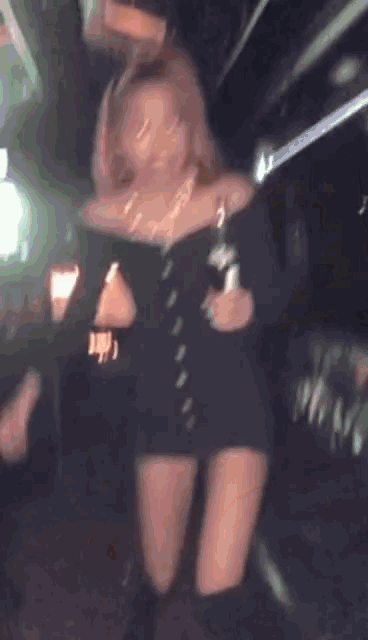 a woman in a black dress is holding a bottle of champagne and dancing .