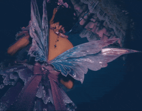 a woman in a purple dress with fairy wings is standing in the dark