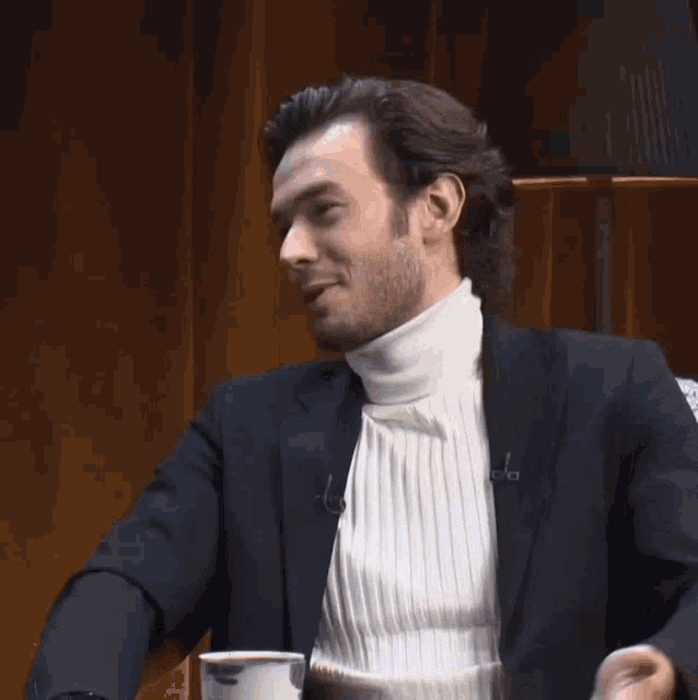 a man wearing a white turtleneck and a black jacket has the letter a on his collar