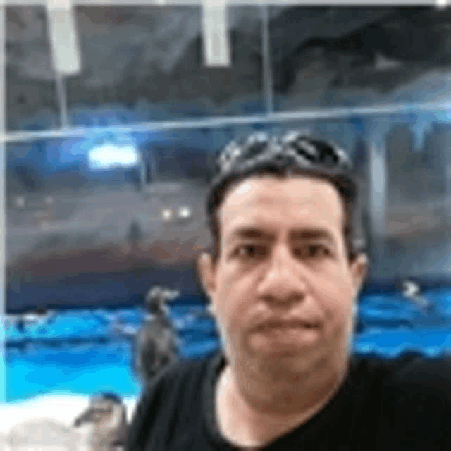 a man wearing sunglasses and a black shirt is taking a selfie in front of a pool .