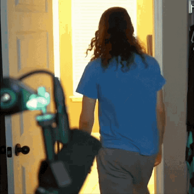 a man with long hair wearing a blue shirt is walking into a room