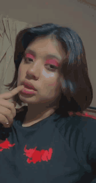 a girl wearing red eye shadow and a black shirt with a red flower on the front