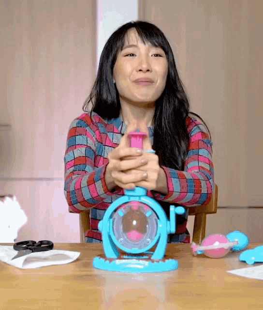 a woman in a plaid shirt is sitting at a table with a toy in front of her