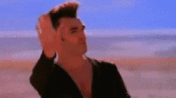 a man is standing on a beach making a funny face with his hands .