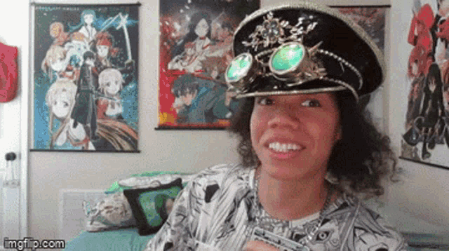 a man wearing a hat and goggles is smiling in front of anime posters on the wall