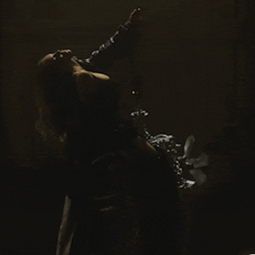 a woman is dancing in a dark room with a fan behind her