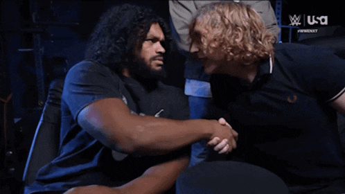 two men shaking hands in front of a screen that says wwe