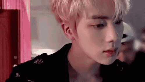 a close up of a young man 's face with a pink curtain in the background .
