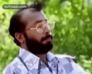 a man with a beard and glasses is smoking a cigarette and looking at the camera .