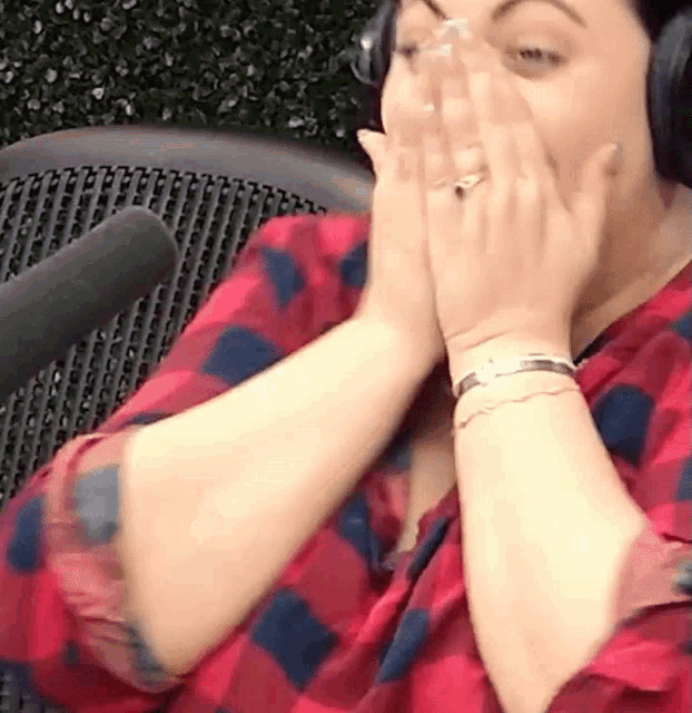 a woman wearing headphones is covering her face with her hands .
