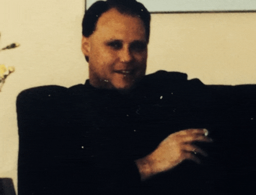 a man in a black shirt is smiling and holding a cigarette