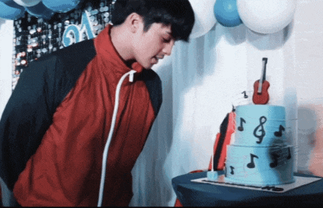 a man blows out a candle on a blue cake with music notes and a guitar on top