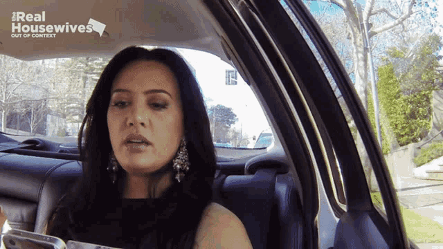 a woman is sitting in a car with the words real housewives out of context behind her