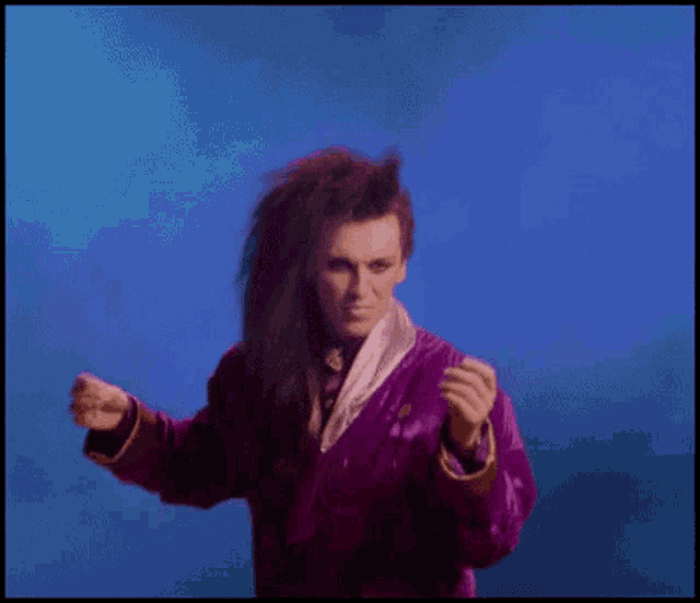a man with long hair and a purple jacket is dancing