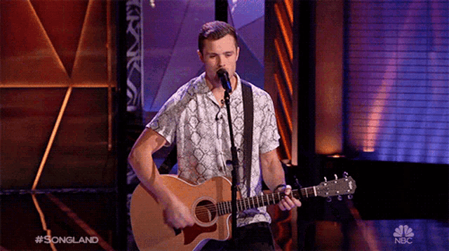 a man singing into a microphone while playing an acoustic guitar on nbc