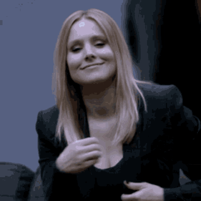 a woman in a black suit is smiling and holding her breast