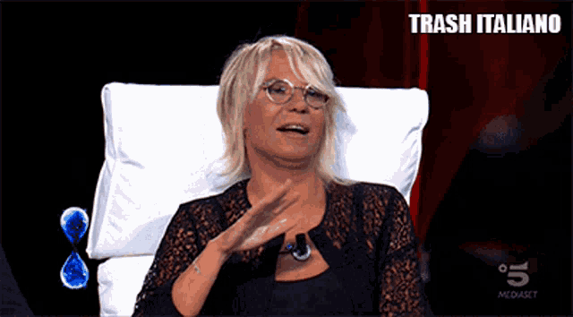 a woman wearing glasses sits in a chair with trash italiano written on the bottom