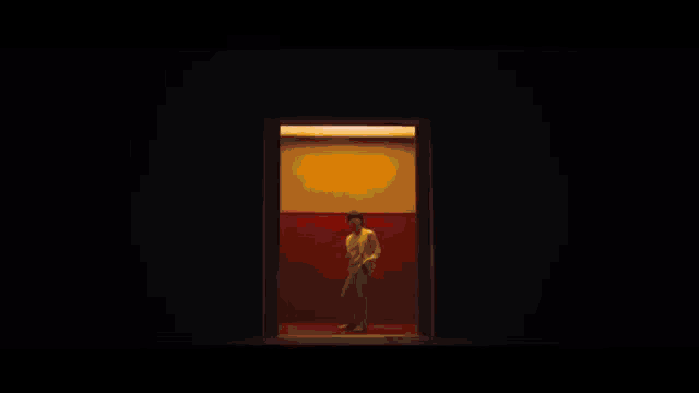 a man in a white suit is standing in front of a red wall in a dark room .