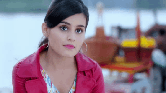 a woman wearing a pink jacket and hoop earrings is looking at the camera