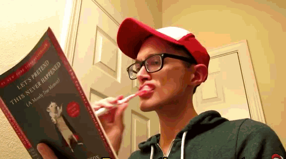 a man is brushing his teeth while reading a book titled let 's pretend this never happened