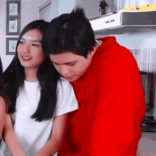 a man in a red hoodie is hugging a woman in a white shirt .